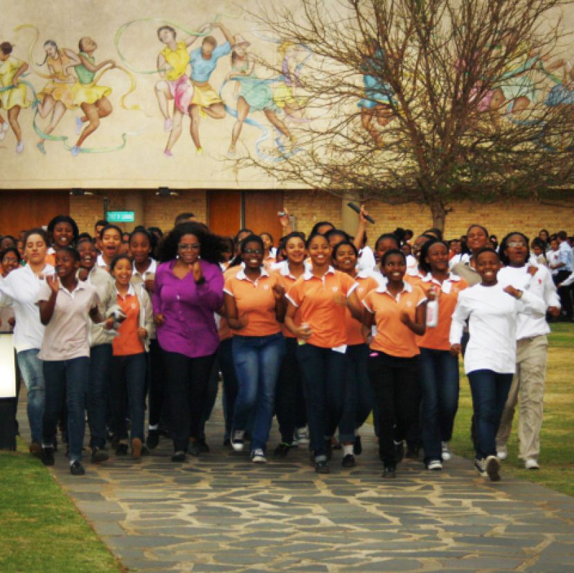 Oprah Winfrey walking briskly with students from the Oprah Winfrey Leadership Academy for Girls in South Africa. They are using Omron pedometers to keep track of their steps, as part of a fittest school challenge